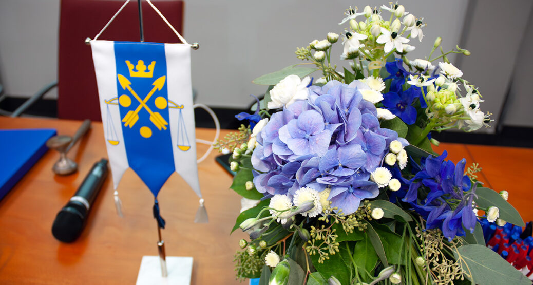 Pöydällä on liiton viiri, kukka-asetelma, mikrofoni ja puheenjohtajan nuija.