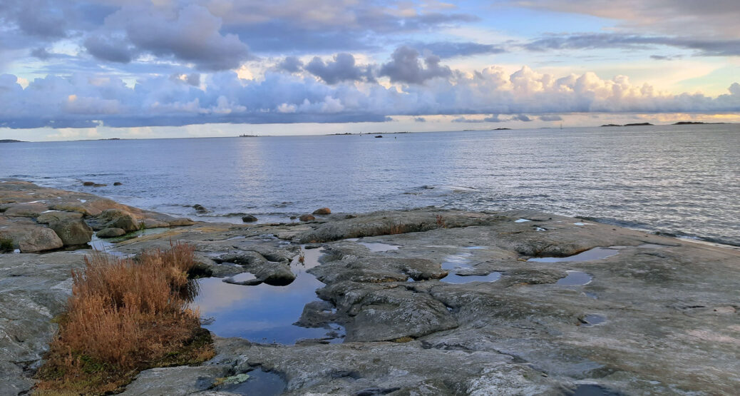 Syksyinen kuva saaristosta. Rantakallioita, tyyni merenpinta. Suuria pilvimuodostelmia horisontissa.